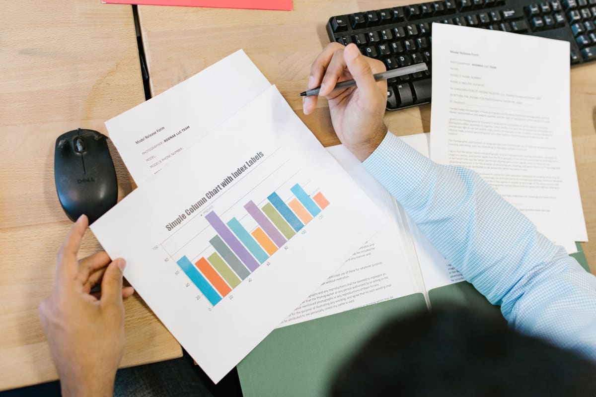Person at a desk reviewing a printed bar chart report with a pen in hand