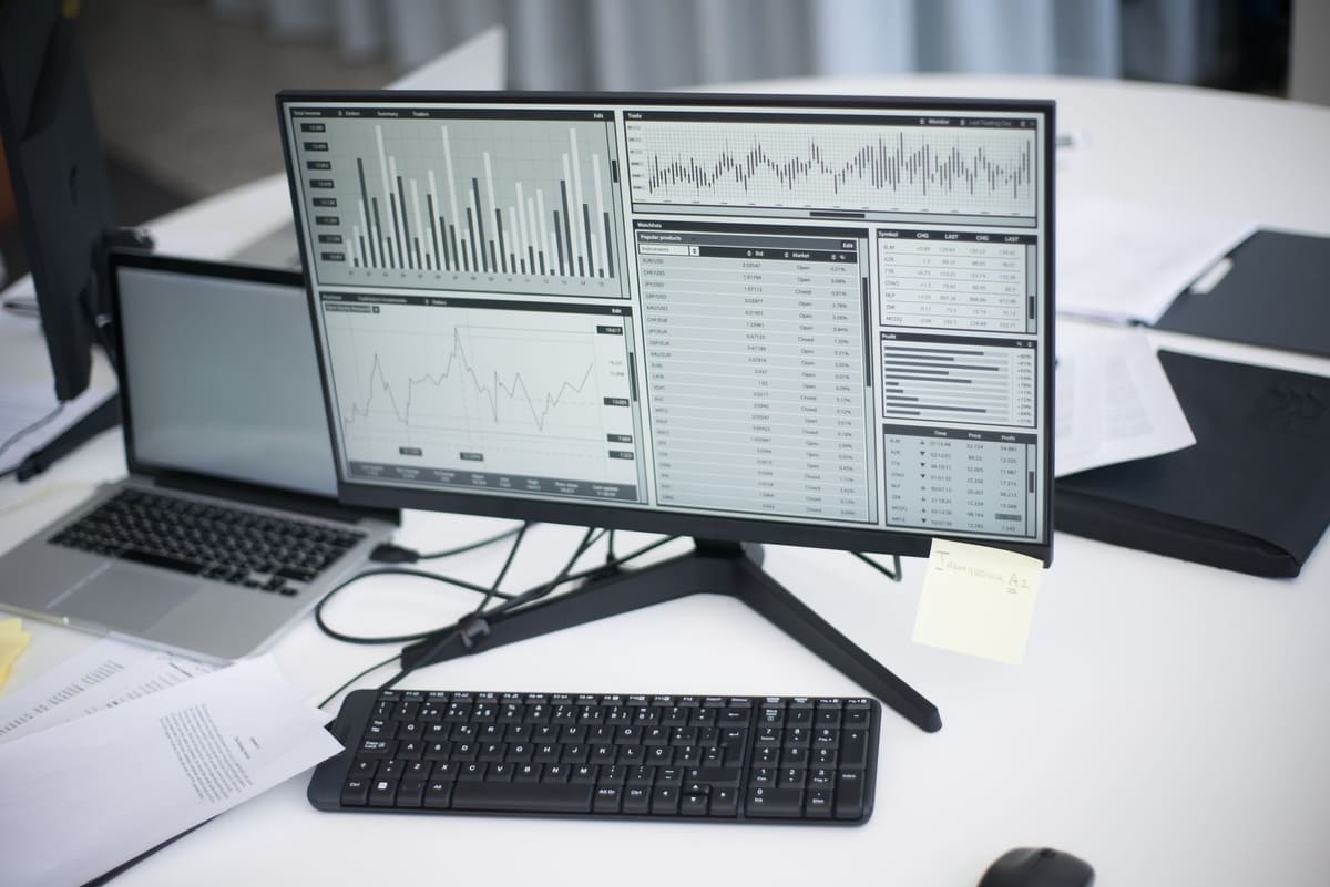 Office desk with a monitor and laptop showing analytics charts and data tables