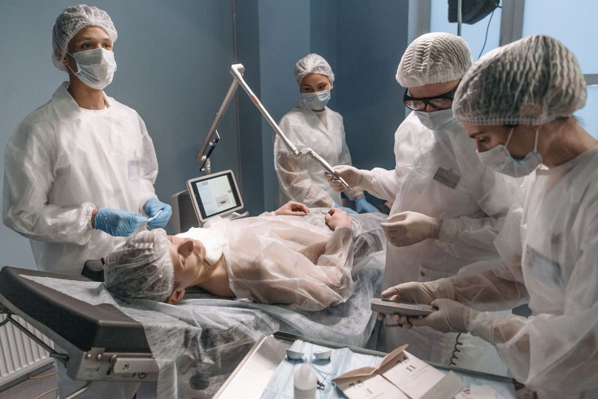Operating room team in caps and masks around a patient, with anesthesia equipment at the head of the table