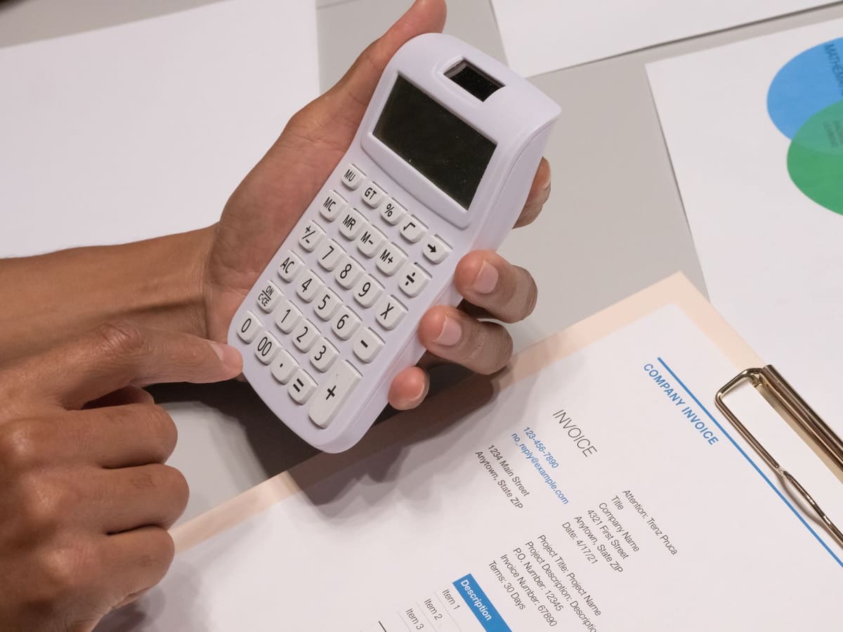 Hands holding a calculator over an invoice on a clipboard