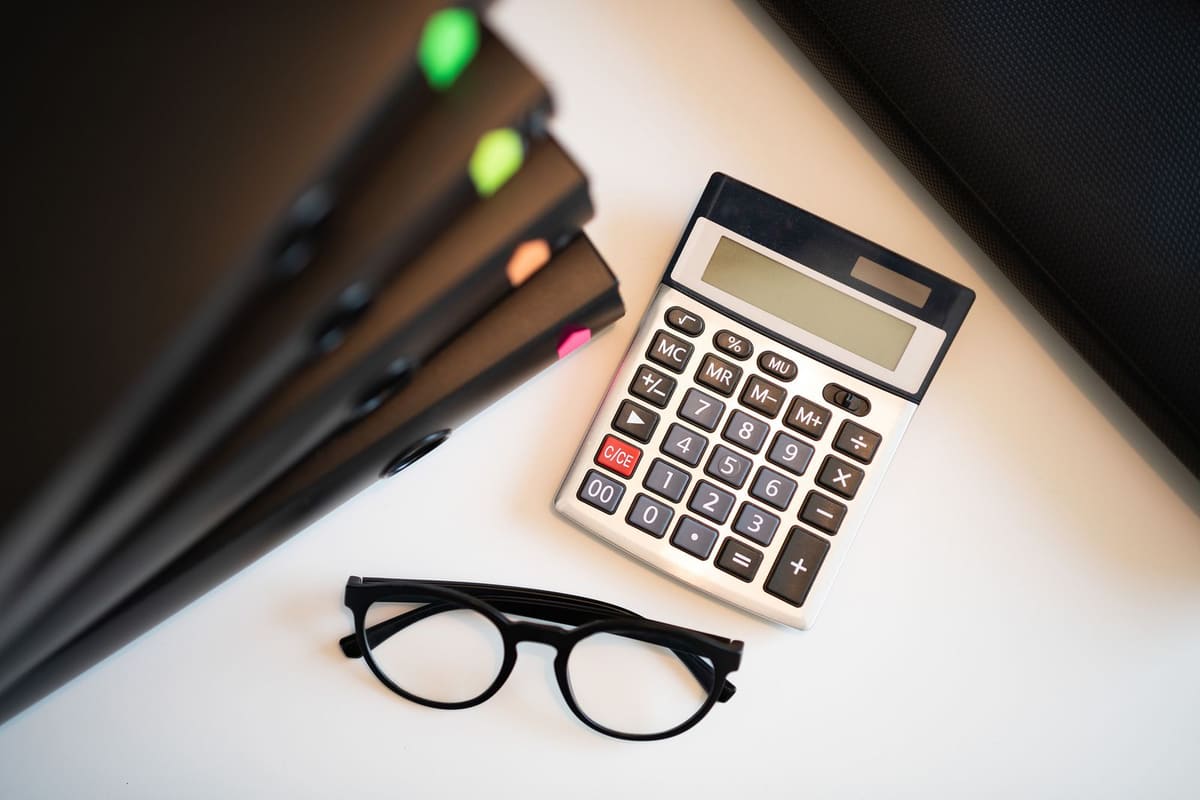 Calculator, eyeglasses and a stack of folders on a white desk