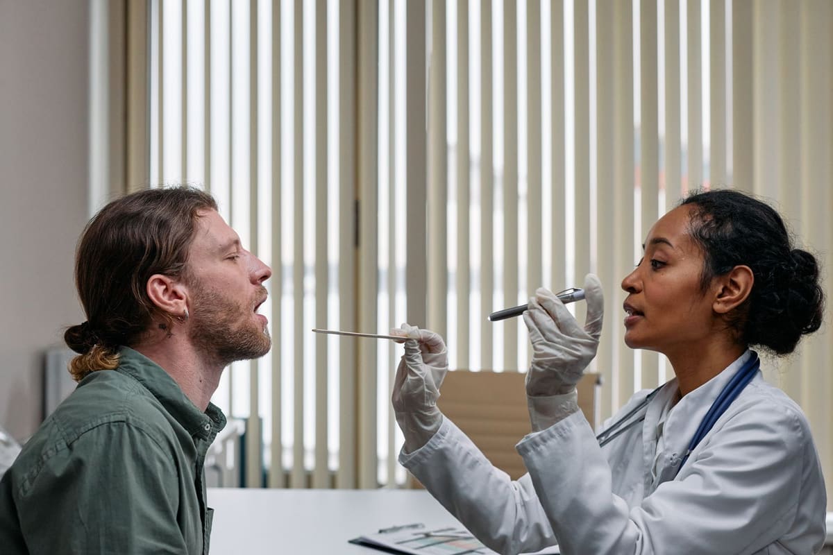 Clinician in gloves examining a patient's throat in an exam room