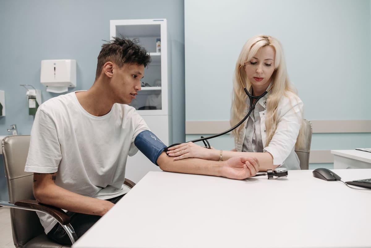 Clinician measuring a patient's blood pressure with a cuff and stethoscope in an exam room