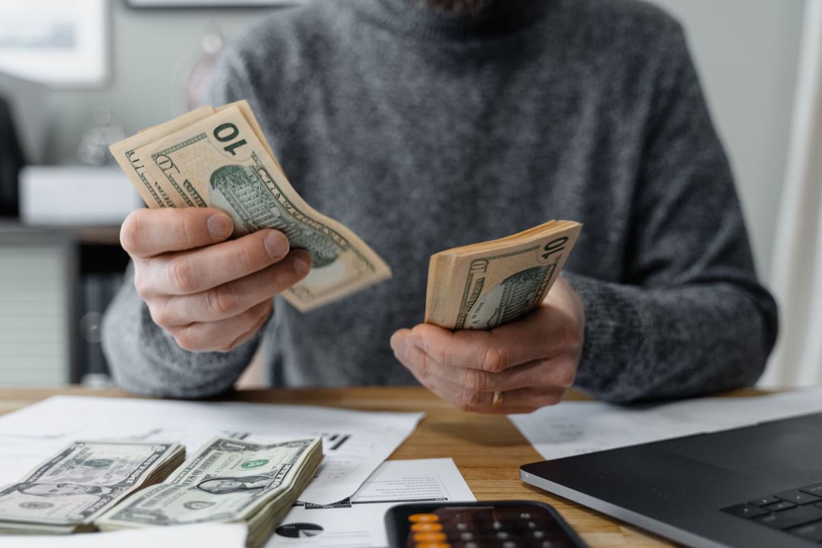 Person counting cash beside a calculator and paperwork