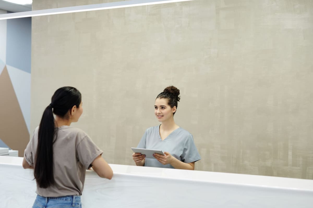 Receptionist with a tablet greeting a patient at a front desk