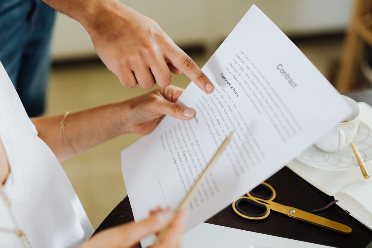 Two people going over a printed contract at a table, one pointing to its commercial terms section