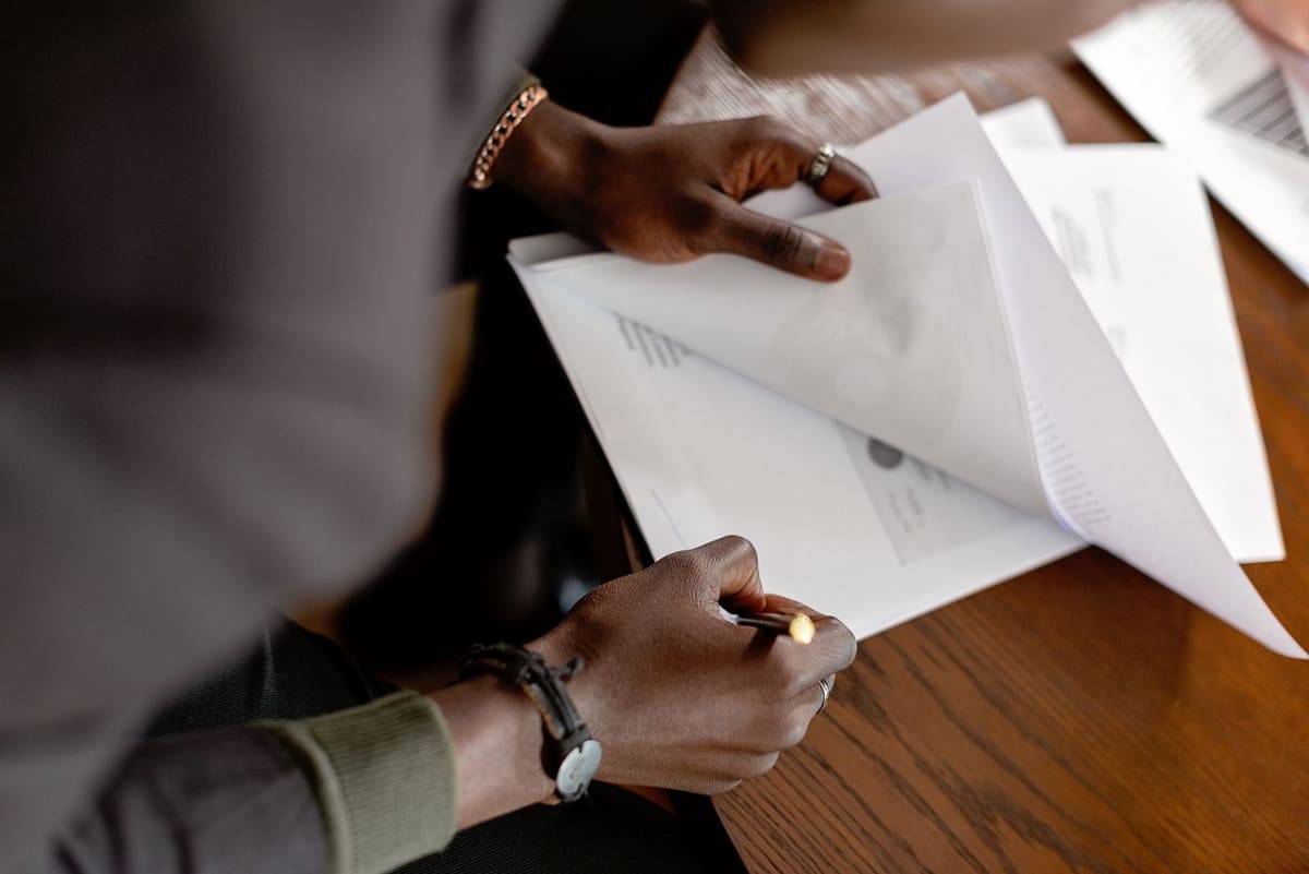 Hands paging through printed documents and marking them with a pen