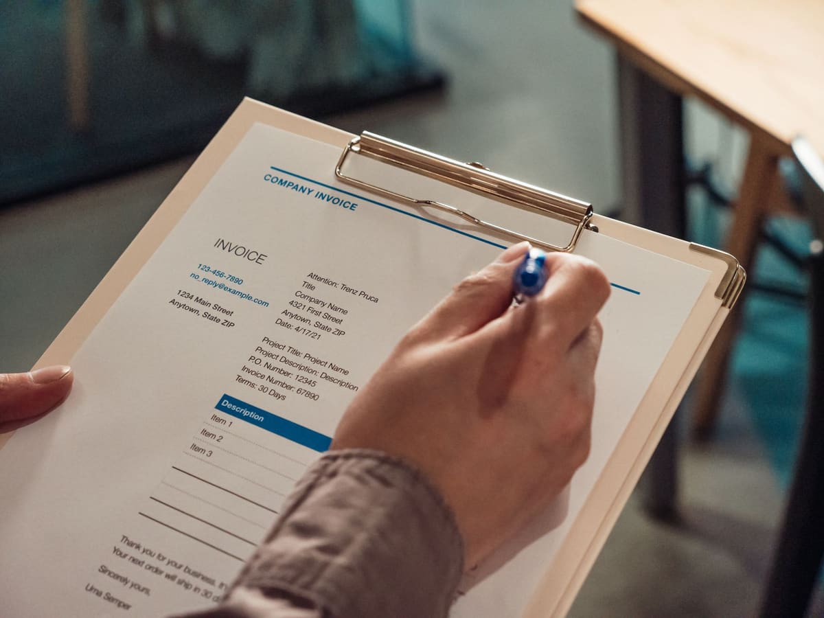 Hand holding a pen over an invoice on a clipboard