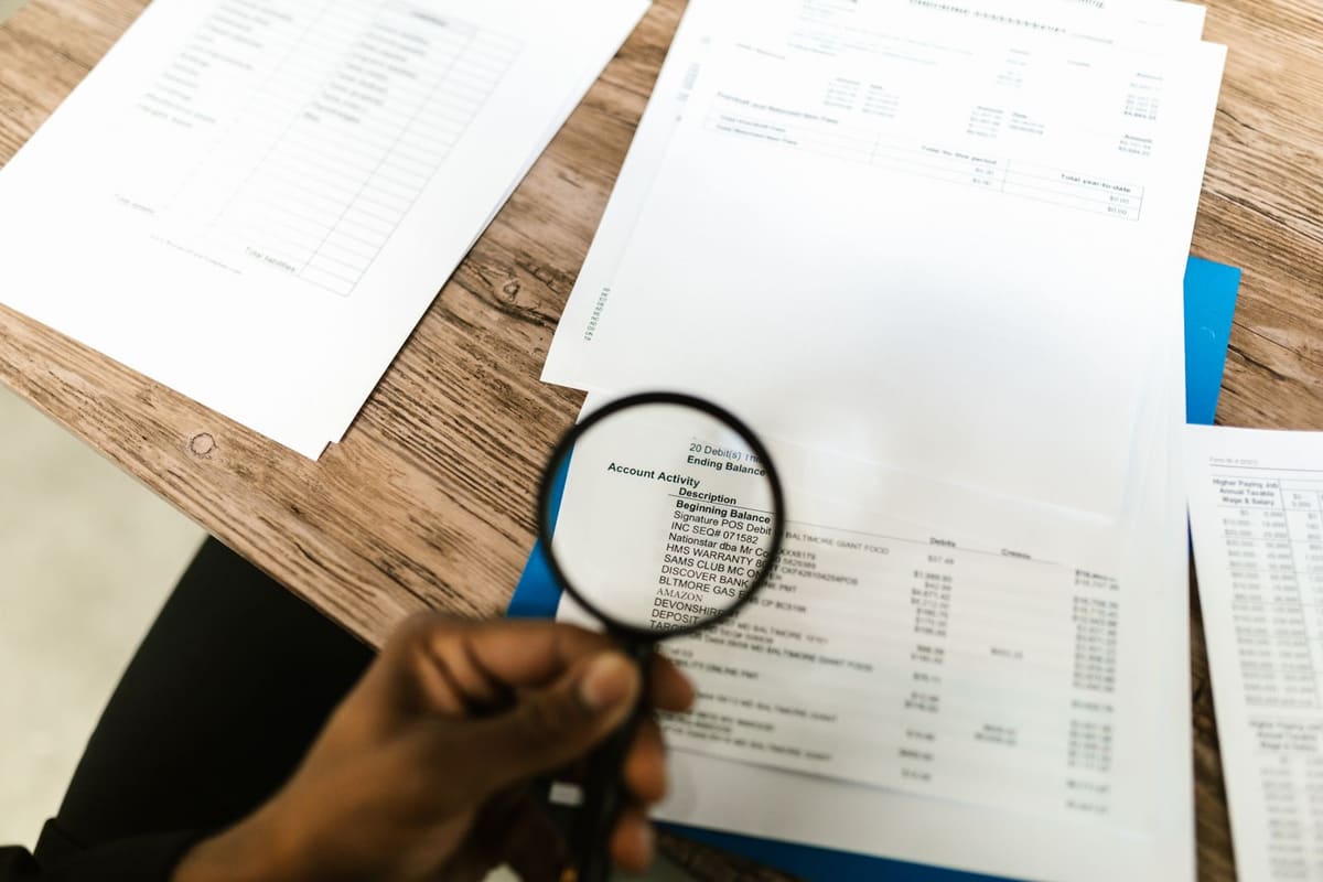 Magnifying glass held over a printed account statement among other financial papers
