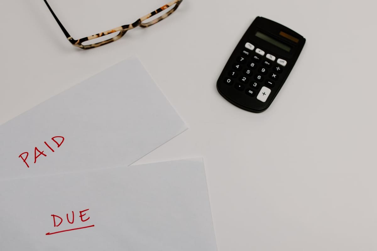 Envelopes marked Paid and Due beside a calculator and reading glasses on a white desk