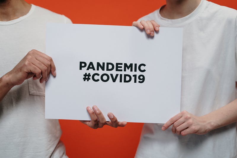 Hands holding a sign that reads Pandemic #COVID19