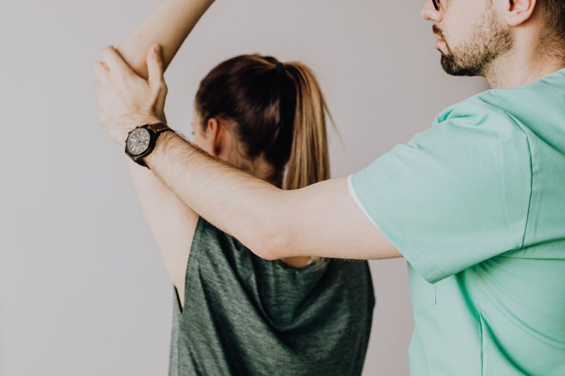 Clinician performing a shoulder and spine mobility evaluation on a patient in an exam room
