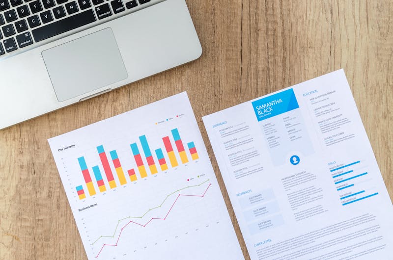Printed charts and reports on a desk beside a laptop