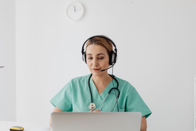 Clinician in scrubs conducting a telehealth appointment with a patient by laptop and headset