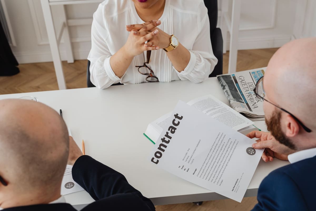 Professionals at a meeting table, one holding a document marked contract
