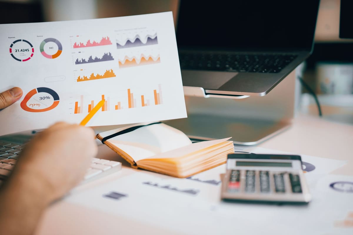 Printed revenue charts and graphs on a desk next to a calculator, like the reports a facility reviews before funding a stipend