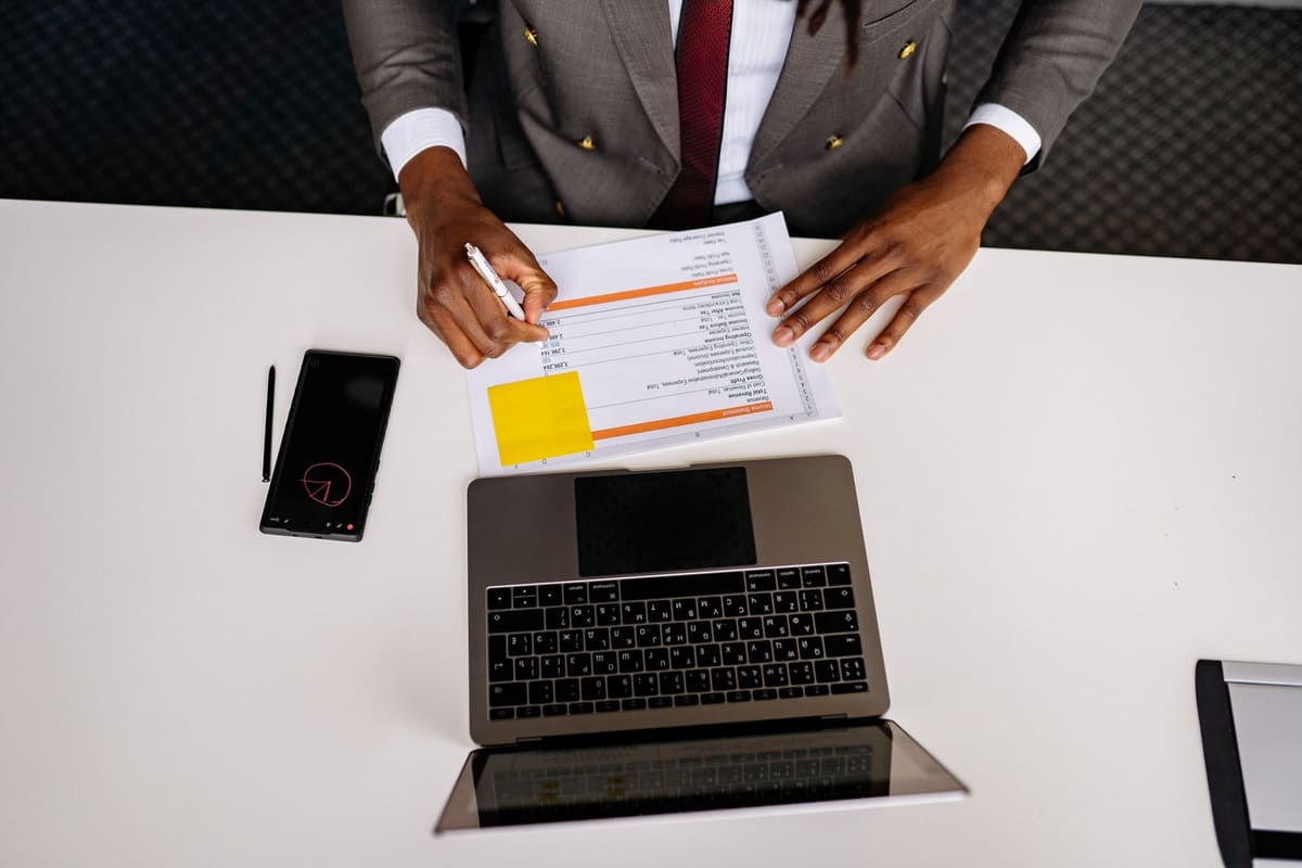 Overhead view of a person pointing to a printed report beside a laptop and phone