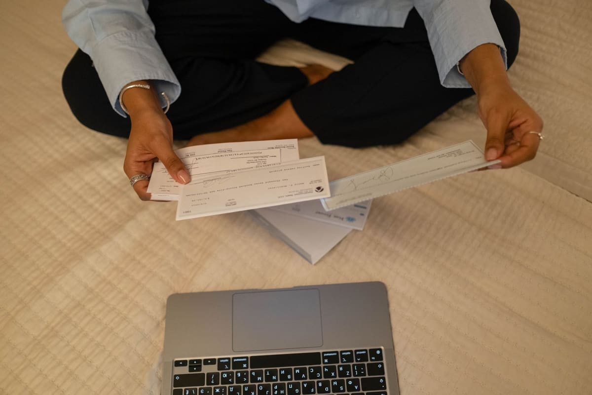 Person sorting paper cheques beside an open laptop
