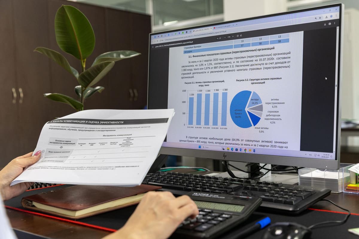 Billing specialist holding a printed form in front of a computer screen of charts and figures