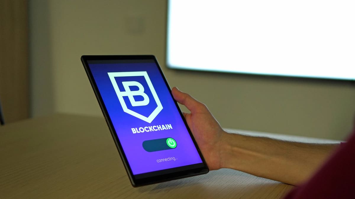 Hand holding a tablet that shows a blockchain app logo